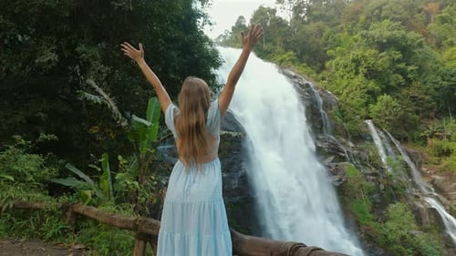 Woman Enjoying View of Majestic Waterfall in Lush Green Forest