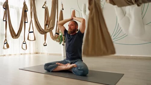 Adult bearded man in sportswear meditating doing breathing exercises during yoga class in the hall