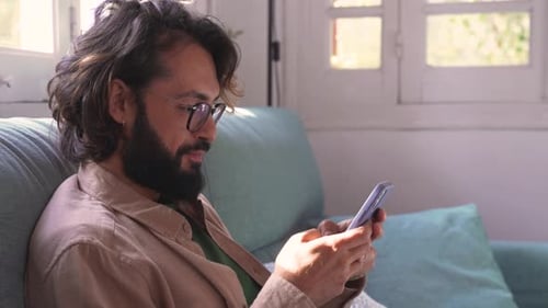 Smiling Man Using Phone While Sitting on Couch