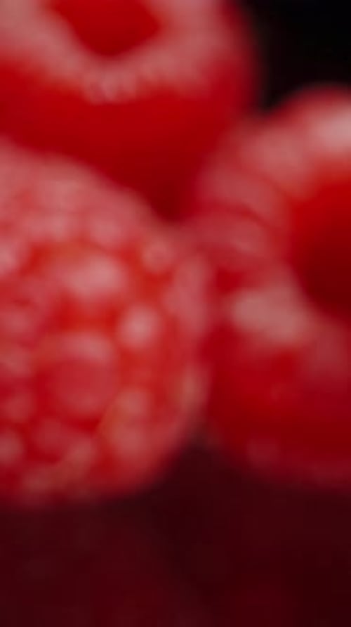 Vertical video. Red raspberries arranged on a black mirrored table. Dolly slider, close up.