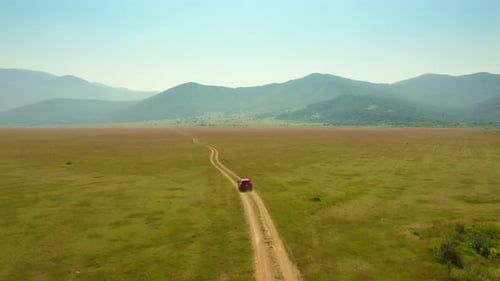 A car drives toward the mountains on a dusty, winding deserted dirt road.