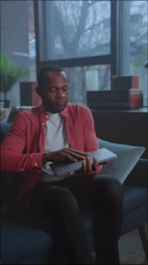 Man Browsing Portfolio Comfortably Seated Man in Warm Living Space Focused on Data on His Portable