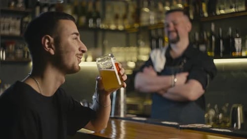 Satisfied Man Drinking Beer at Bar Bartender Smiling in Background