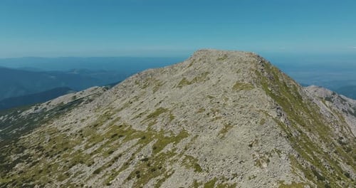 Rocky mountain tall peak on a clear sunny day with blue skies and vibrant green grass, rising drone