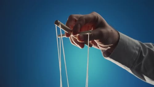 La mano de un hombre con una camisa gris controla una marioneta con un manipulador de madera y cuerdas en un azul