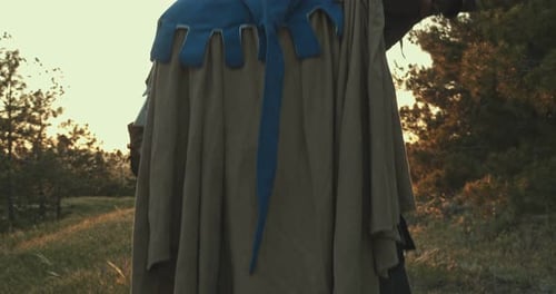 A Man in a Medieval Knight Costume Stands in a Forest with a Sword Above His Head Against the
