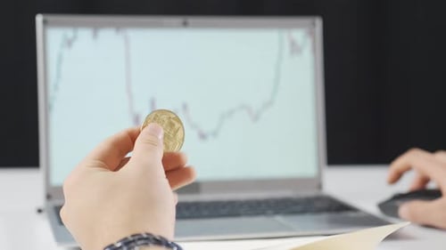 Hands Holding Bitcoin Coin in Front of Stock Chart
