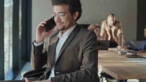 Biracial Young Man in Wheelchair Talking on Mobile at Team Meeting in Office