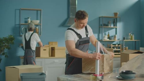 Workers of Moving Company With Uniforms Carefully Packing Things at Boxes