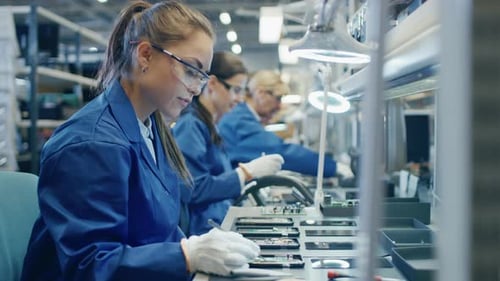 Arbeiterin in einer Elektronikfabrik in blauem Arbeitsmantel und Schutzbrille montiert gedrucktes Ci