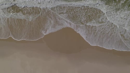 Aerial top-down shot of the beautiful generic sandy beach, bird's eye view of ocean waves crashing a