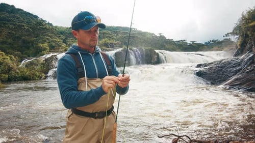 Man Prepares Fishing Rod on Rushing River