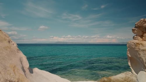 Ruhige türkisfarbene Meerwasseroberfläche mit Felsen und Wolkenlandschaft