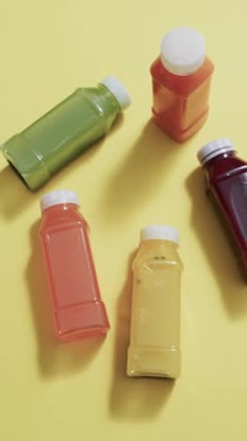 Vertical video of bottles of fruit juice with copy space over yellow background