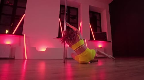 Young Woman Performing Sensual Pole Dance in Studio with Red Lightstands