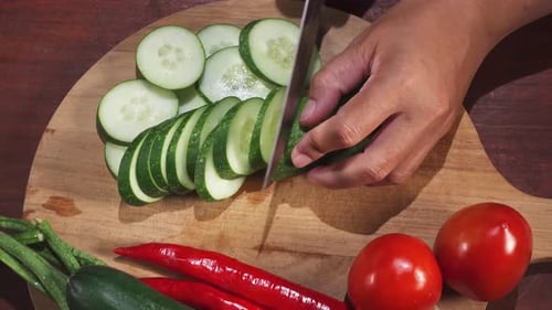 Green cucumbers are cut with a knife on wooden cutting board