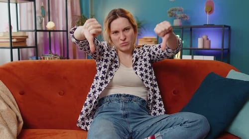 Woman Gives Thumbs Down Gesture While Sitting on Couch