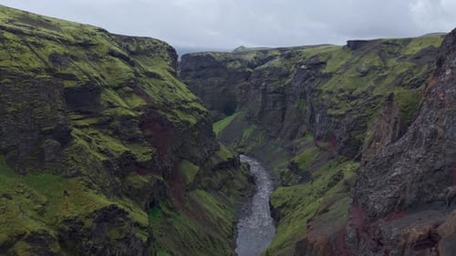 Breathtaking flyover of emerald green moss clinging to dark, rocky canyon walls.