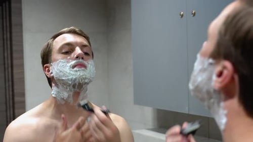 Man Shaving His Beard in the Bathroom Mirror