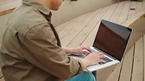 Homme asiatique utilisant un ordinateur portable en plein air, gros plan, jeune homme coréen, travaillant à distance sur un ordinateur dans la rue