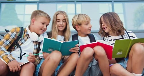 Close up of four caucasian school friends talking and doing homework, having fun during break