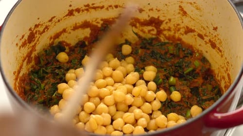 Adding Chickpeas to Vegetable Dish in Red Pot