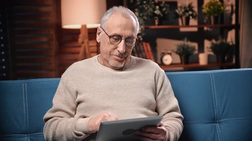 Senior Man Using Tablet on Blue Couch