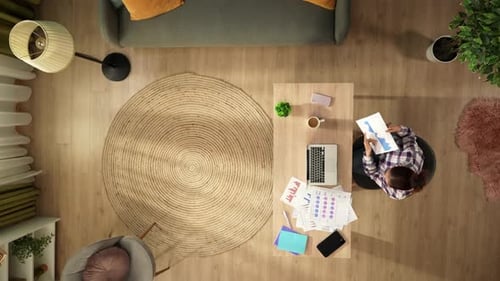 Top View Capturing a Woman Having a Videocall on a Laptop in Her Home Office Discussing Graphs and