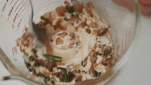 Mixing vegetable sauce ingredients with mayonnaise inside measure glass bowl.
