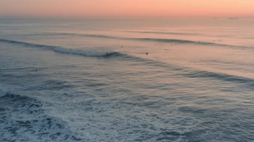 Beautiful aerial view of surfer surfing a perfect wave at sunset / sunrise. Amazing ocean swell.