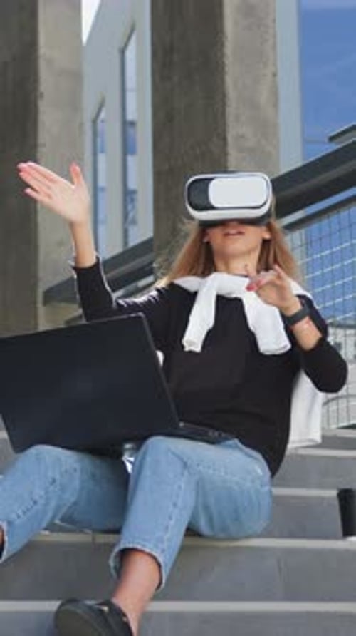 Woman Sits with Laptop Using VR Headset Outdoors