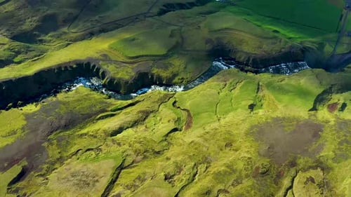 Winding glacial river gorge cutting through bright green rolling hills landscape