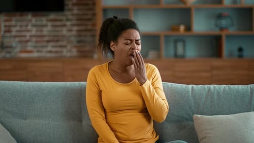 Woman in Yellow Sweater Yawning While Sitting on Sofa in Living Room