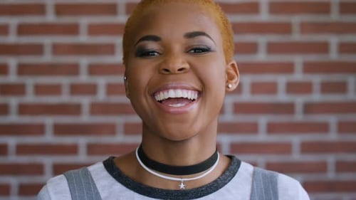 Face, laughing and black woman, student and gen z on brick wall background at campus excited