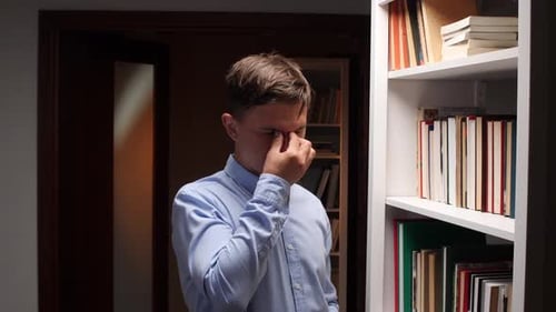 Tired Office Worker Rubbing Eyes Near Bookshelf