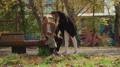 Parents Guide Child Outdoors Happily Child Begins Walking Amid Park Playfulness and Smiles Family