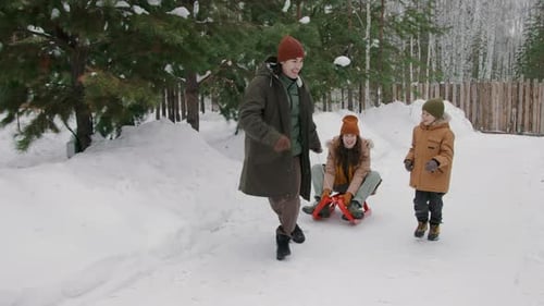 Laughing Young Father and Son Giving Mom Ride on Sledge in Snow