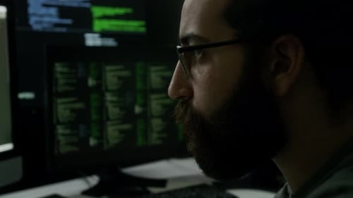 Programmer Intensely Watching Running Lines of Code on Multiple Monitors