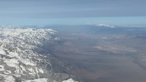 Une large prise de vue aérienne suit la colonne vertébrale d'une chaîne de montagnes très enneigée : les sommets déchiquetés et