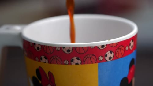 A cup of coffee being poured into a cup, with a close-up of a coffee cup featuring soccer balls