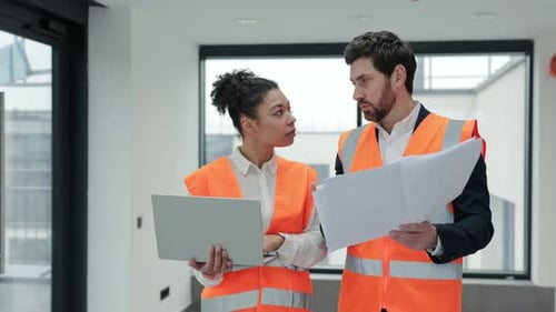 Diverse Architects Discuss Blueprints and Laptop at Construction Site