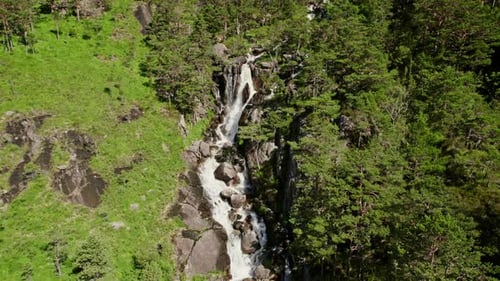 Waterfall Cascading Amidst Rocky Slopes And Verdant Greenery