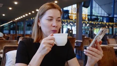 Woman Drinks Coffee and Uses Phone at Cafe