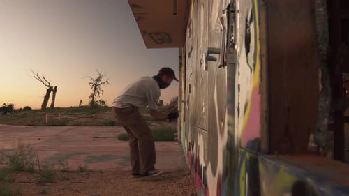 Artista de rua pintando com spray parede de prédio abandonado ao pôr do sol