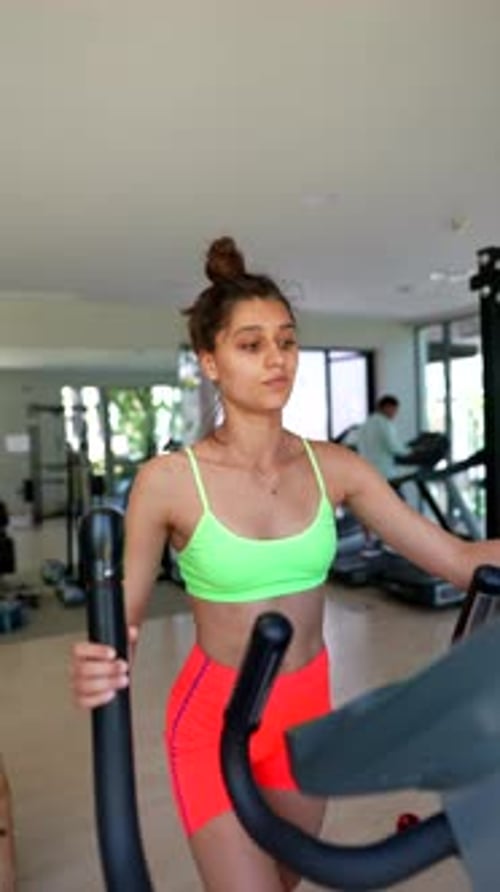 A Woman is Focused on Her Fitness Goals Using an Elliptical Machine in a Modern Gym