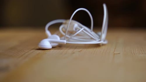 Los auriculares intraurales blancos con cable y conector auxiliar se colocan sobre una tabla de madera clara y giran