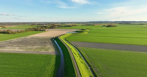 Aerial view of a winding road on a dam surrounded by fresh green fields. Drone video.