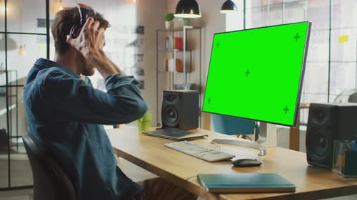 Junger professioneller kreativer Mitarbeiter arbeitet an seinem PC mit großem Greenscreen-Mock-Up D