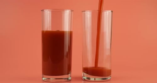 Le jus de tomate est versé dans des gobelets en verre sur fond rose. Ralenti.