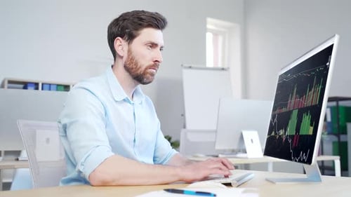 Confident business man stocks broker sitting in front of monitor screen in office analyzing stat